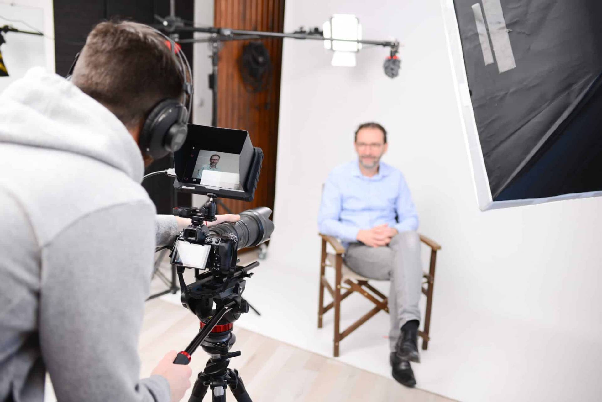 Man being interviewed by camera operator with monitor on a set